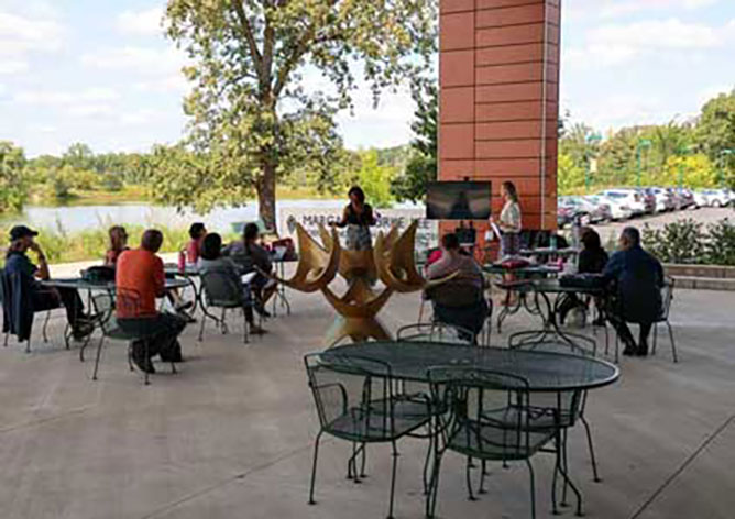 Appears to be faculty and staff sitting outside at the Lee Center patio listening to a lecture.